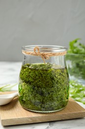 Photo of Jar of tasty arugula pesto on white table