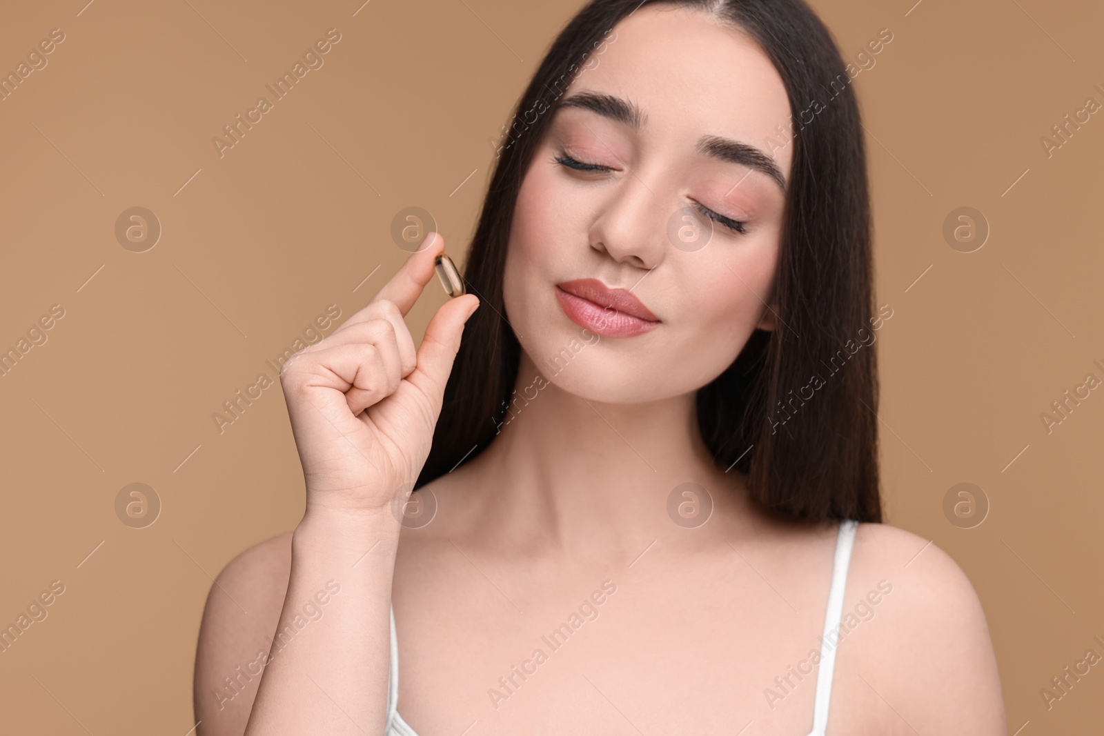 Photo of Beautiful young woman with vitamin pill on beige background