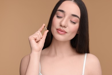 Beautiful young woman with vitamin pill on beige background