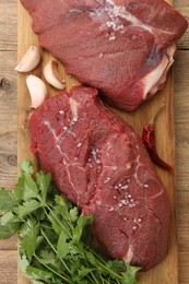 Pieces of raw beef meat, parsley, garlic and spices on wooden table, top view