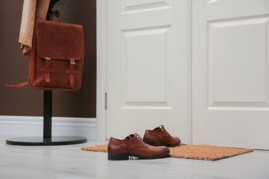 Photo of Stylish shoes on door mat near coat rack in hall