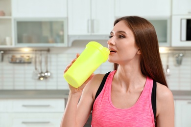 Photo of Young woman drinking protein shake in kitchen