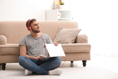 Photo of Young man with headphones and laptop sitting on floor in living room