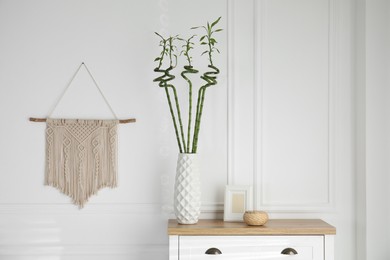 Photo of Vase with green bamboo stems on chest of drawers in room. Interior design