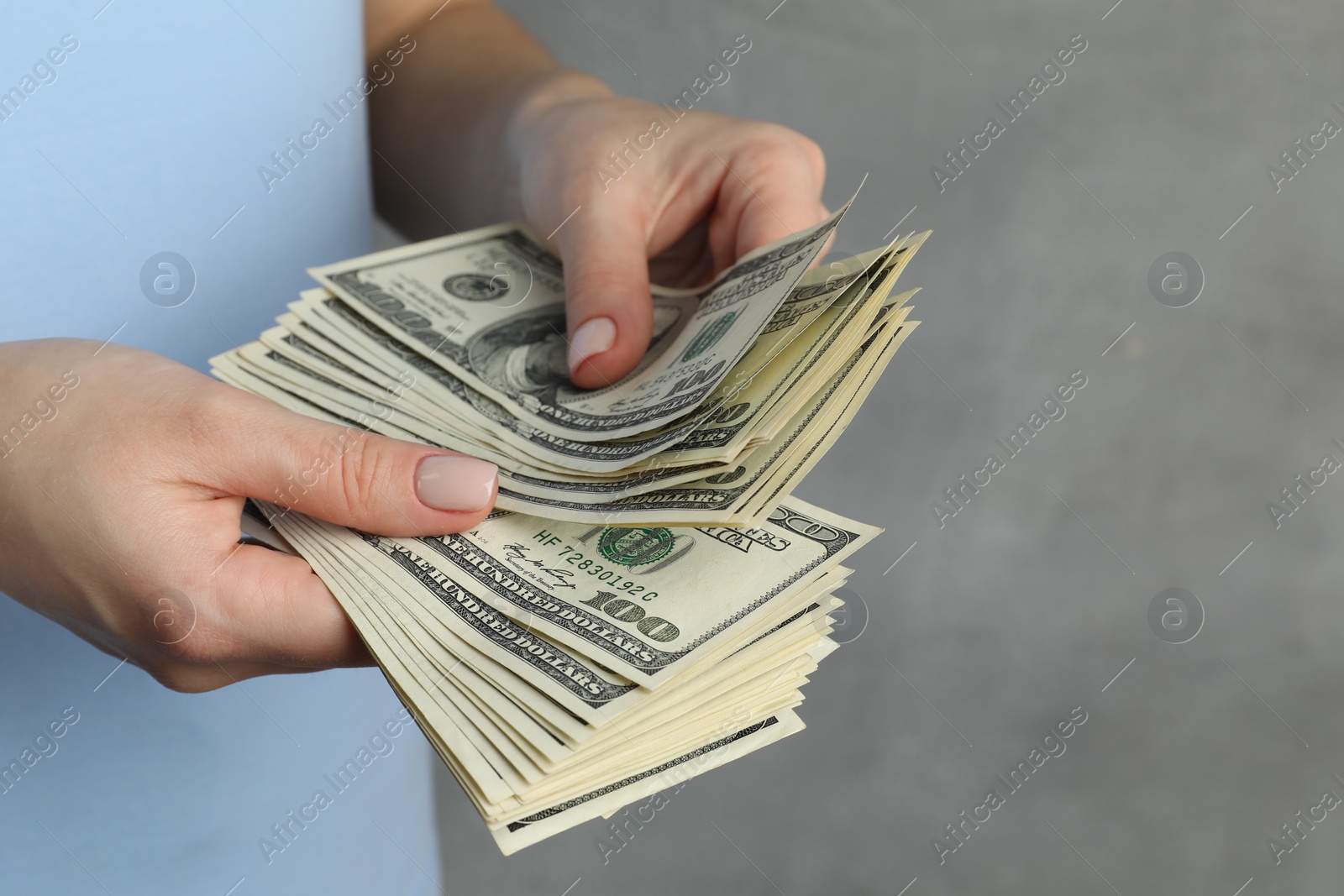 Photo of Money exchange. Woman counting dollar banknotes on grey background, closeup. Space for text