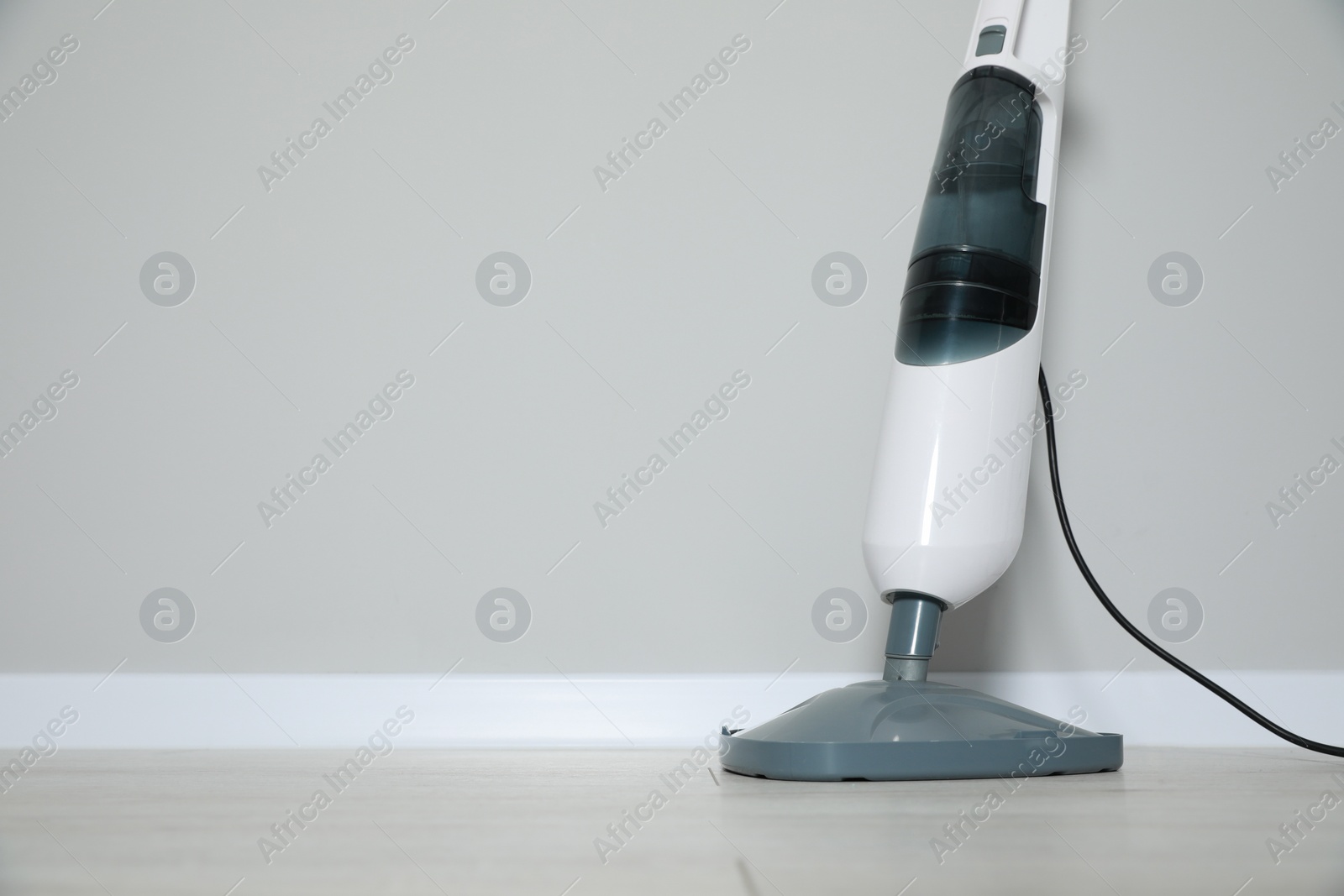 Photo of One modern steam mop on floor near grey wall, space for text