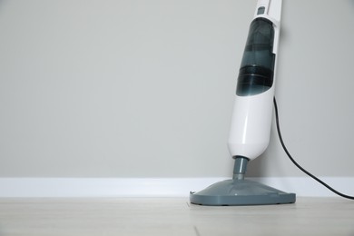 Photo of One modern steam mop on floor near grey wall, space for text