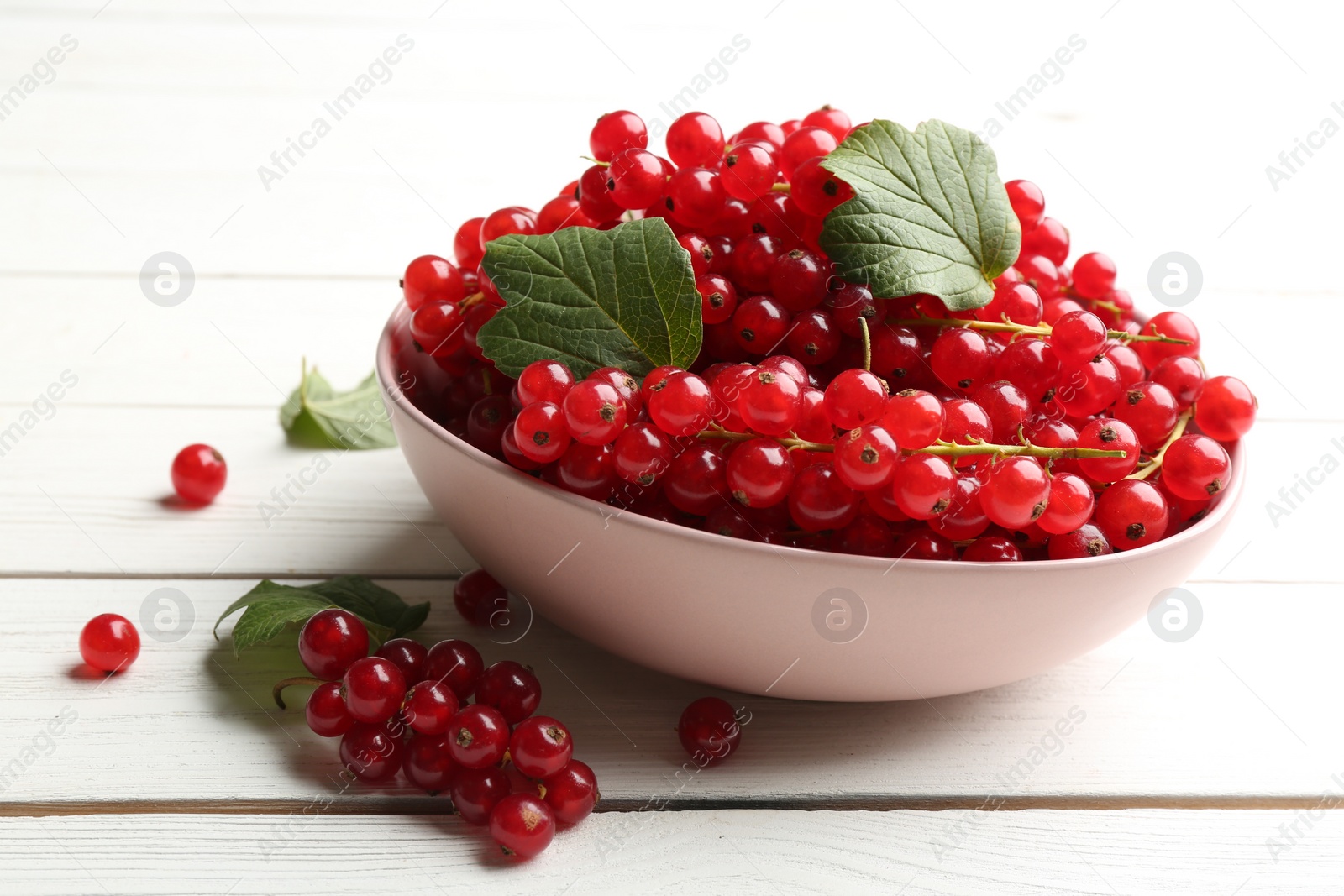 Photo of Delicious red currants and leaves on white wooden table
