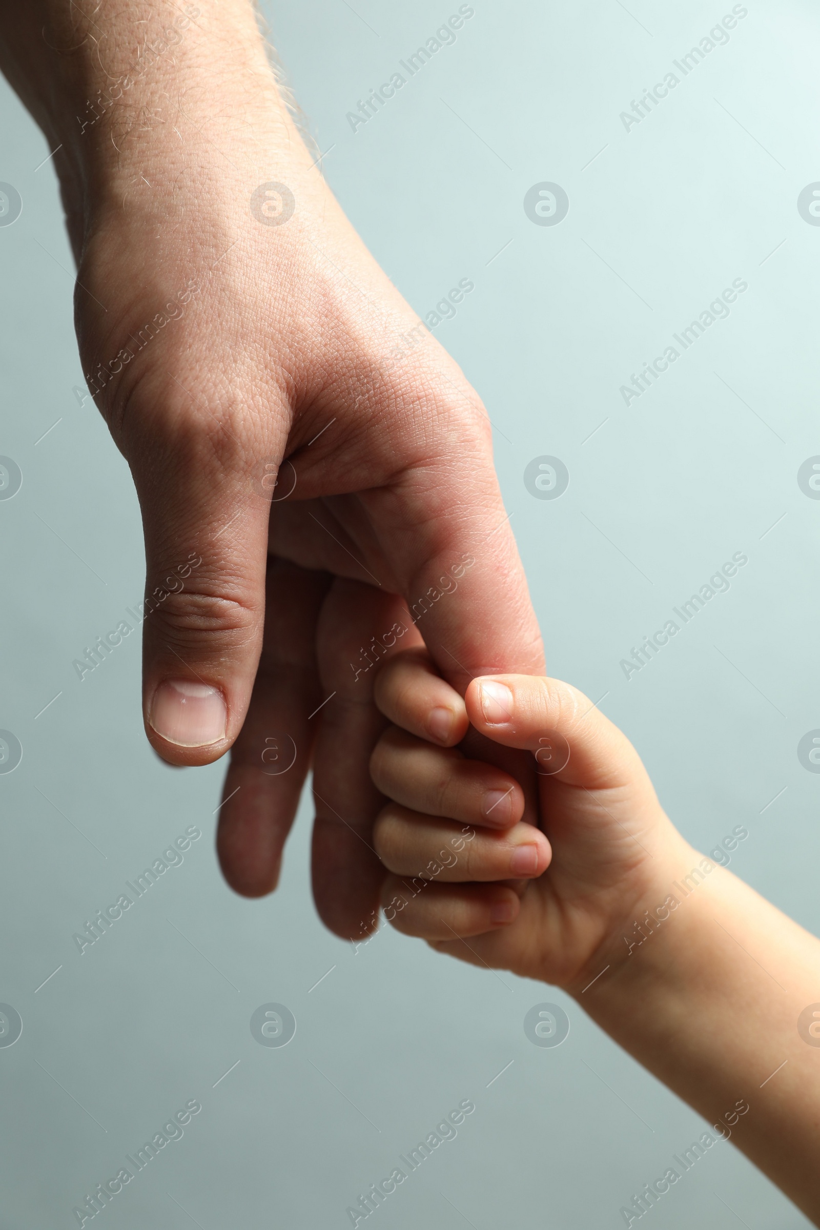 Photo of Father and child holding hands on light blue background, closeup