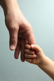 Photo of Father and child holding hands on light blue background, closeup