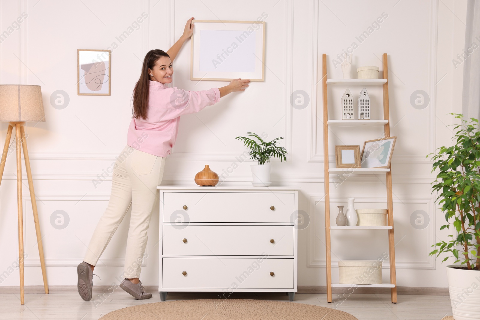 Photo of Woman hanging picture frame on white wall at home