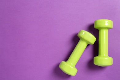 Photo of Bright dumbbells on violet background, flat lay. Space for text