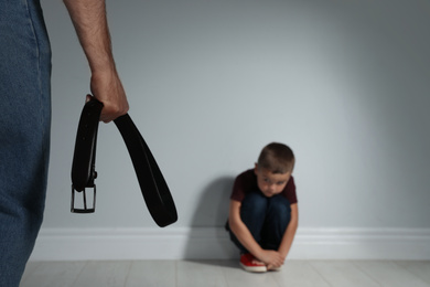 Photo of Man threatening his son with belt indoors. Domestic violence concept