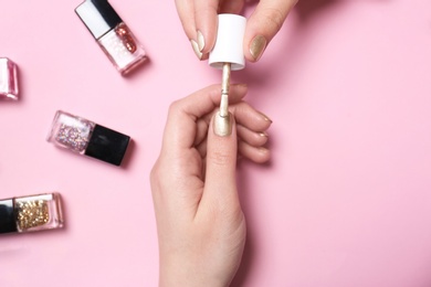 Woman applying nail polish on color background, top view