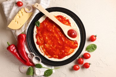 Pizza base smeared with tomato sauce and products on light textured table, flat lay