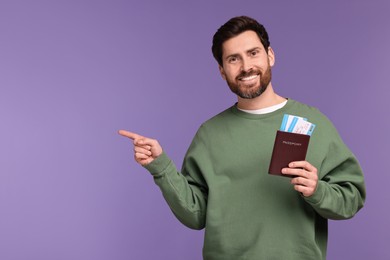 Smiling man with passport and tickets pointing at something on purple background. Space for text