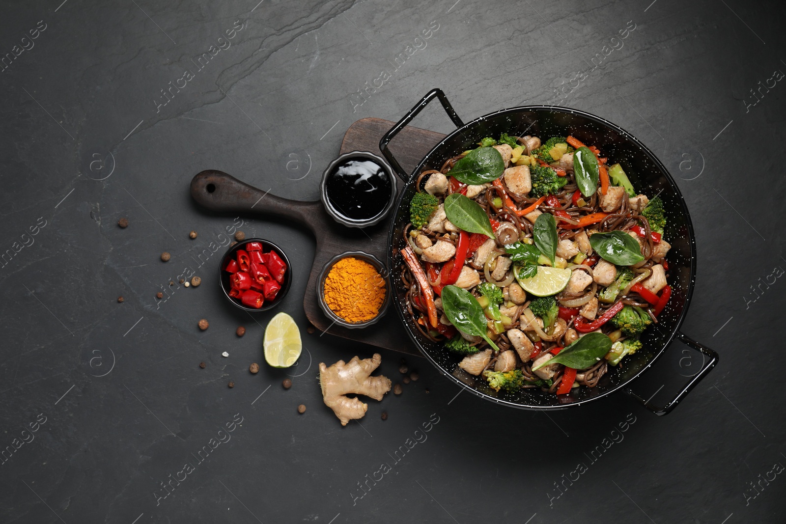 Photo of Stir-fry. Tasty noodles with meat in wok and ingredients on grey textured table, flat lay