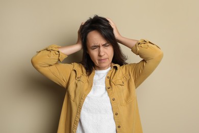 Mature woman suffering from headache on beige background