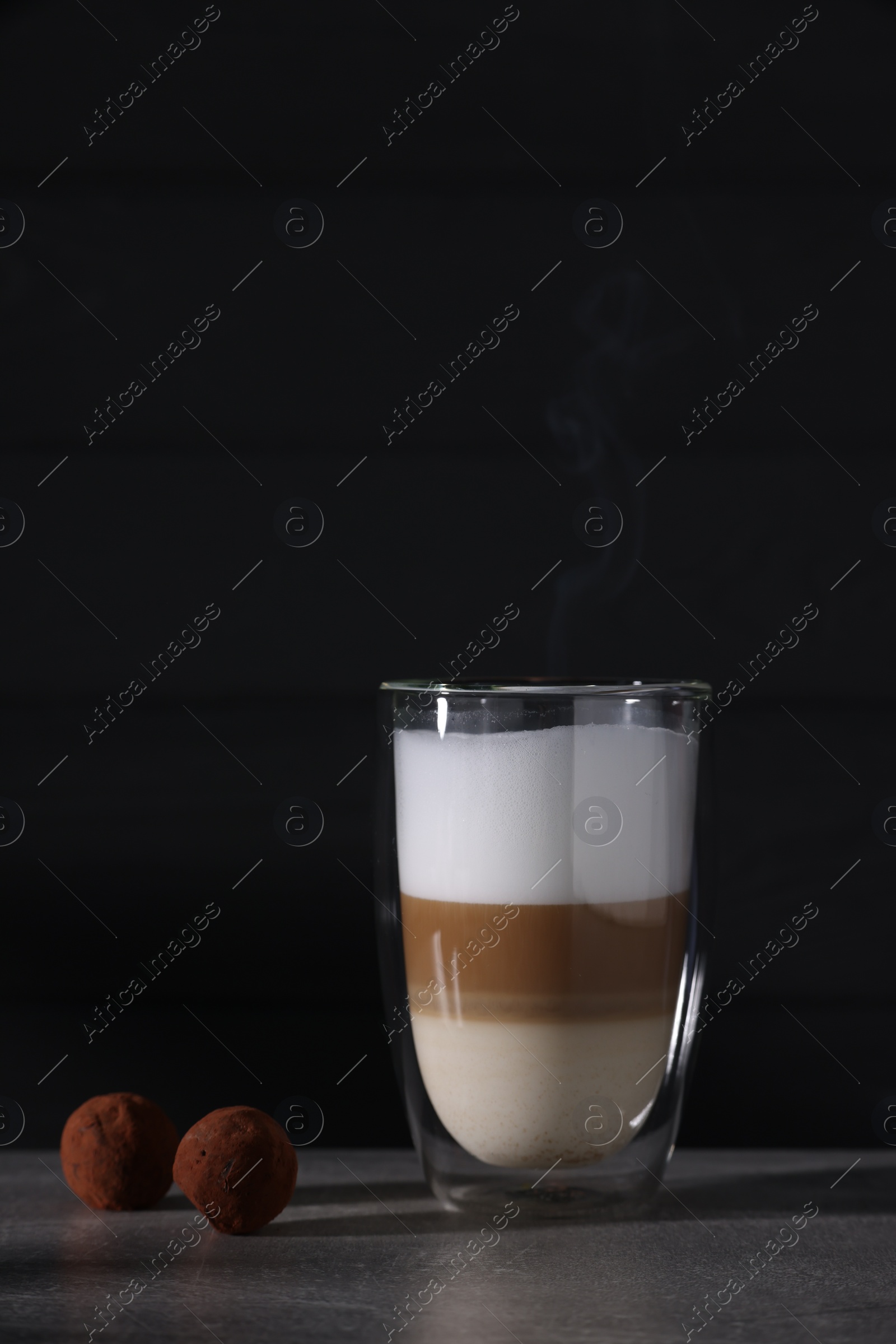 Photo of Aromatic latte macchiato in glass and chocolate candies on grey table against black background