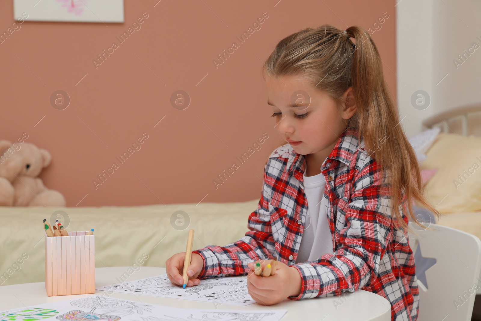 Photo of Little girl coloring antistress page at table indoors