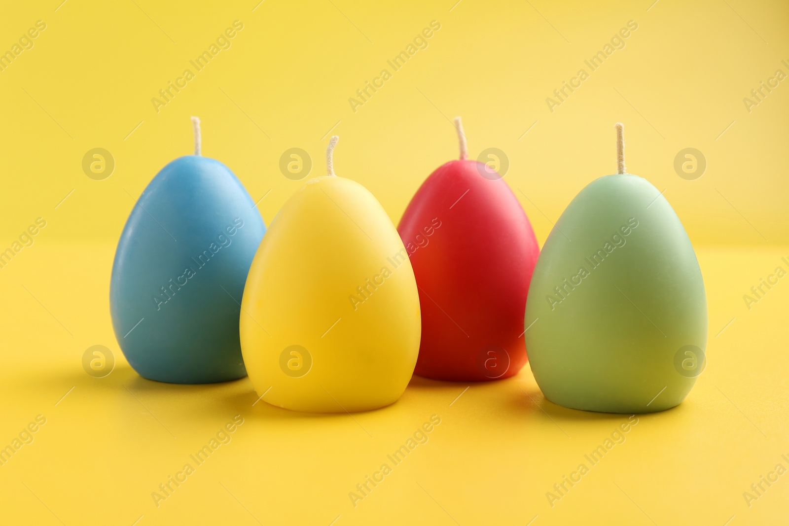 Photo of Colorful egg shaped candles on yellow background. Easter decor