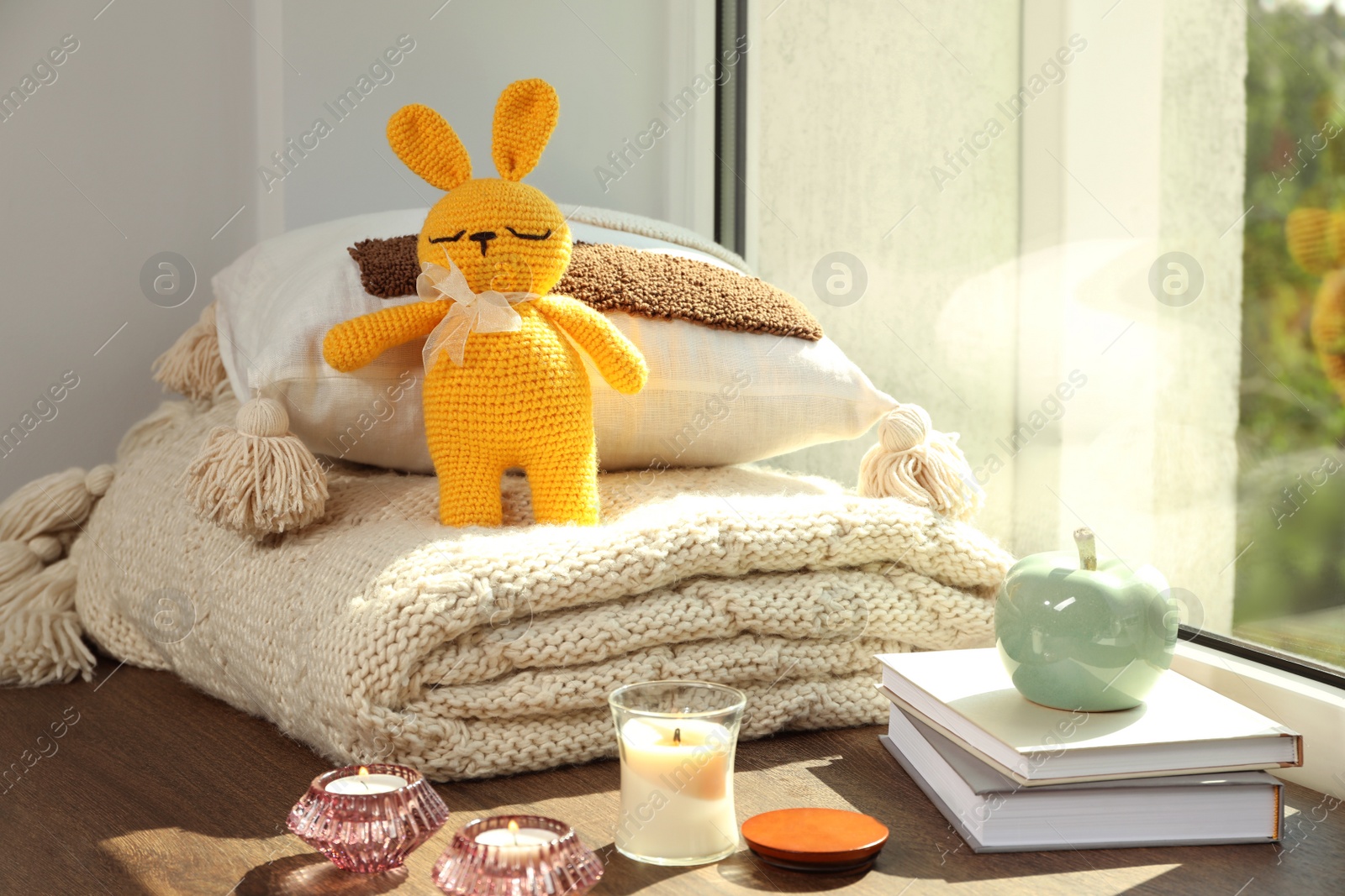 Photo of Knitted bunny toy, pillow, plaid and home decor on wooden window sill