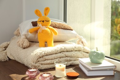 Photo of Knitted bunny toy, pillow, plaid and home decor on wooden window sill