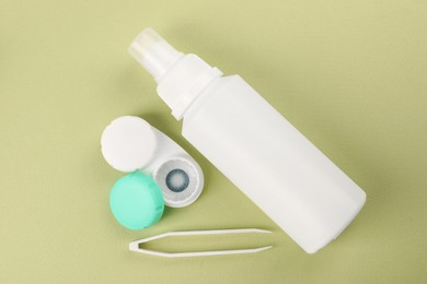 Photo of Case with blue contact lenses, bottle of cosmetic product and tweezers on light green background, flat lay