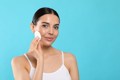 Photo of Young woman using cotton pad with micellar water on light blue background, space for text