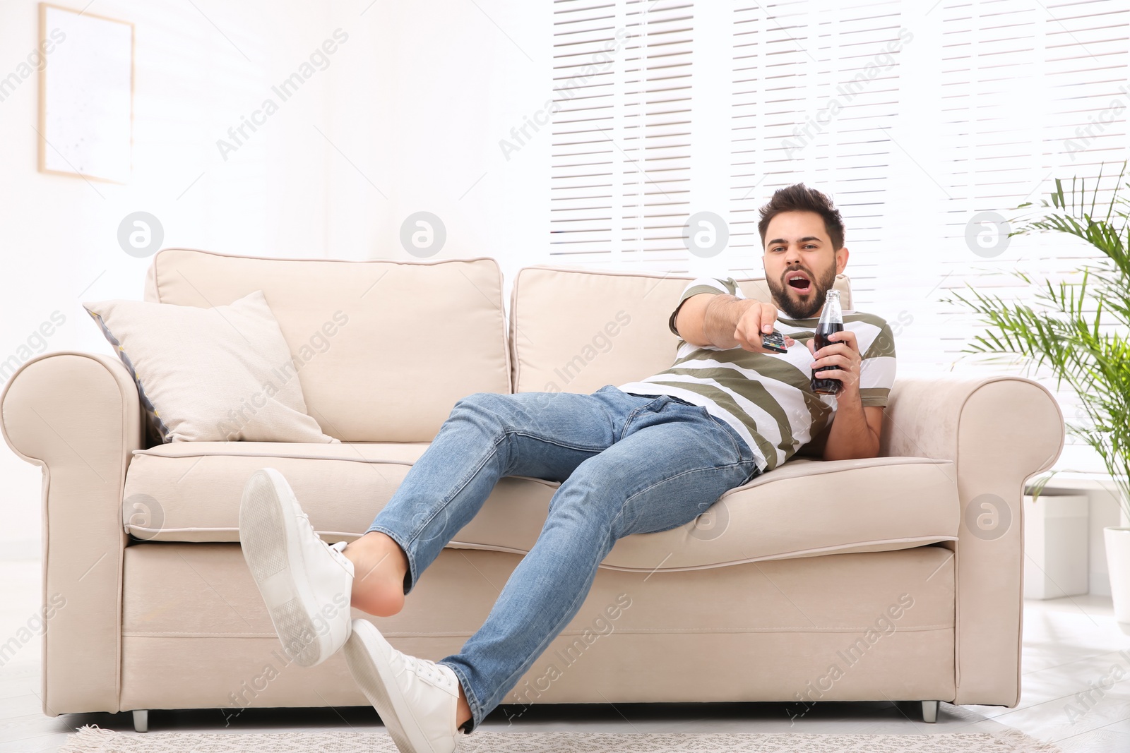 Photo of Lazy young man watching TV on sofa at home