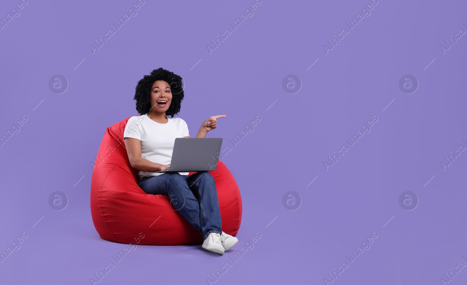 Photo of Happy young woman with laptop sitting on beanbag chair against purple background. Space for text