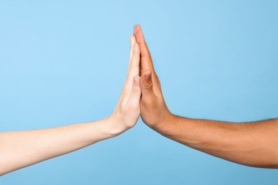 Photo of International relationships. People giving high five on light blue background, closeup