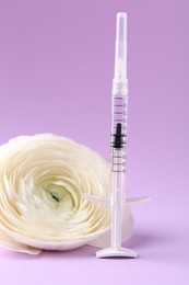 Photo of Cosmetology. Medical syringe and ranunculus flower on violet background