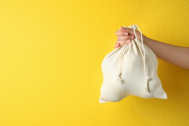 Woman holding full cotton eco bag on yellow background, closeup. Space for text