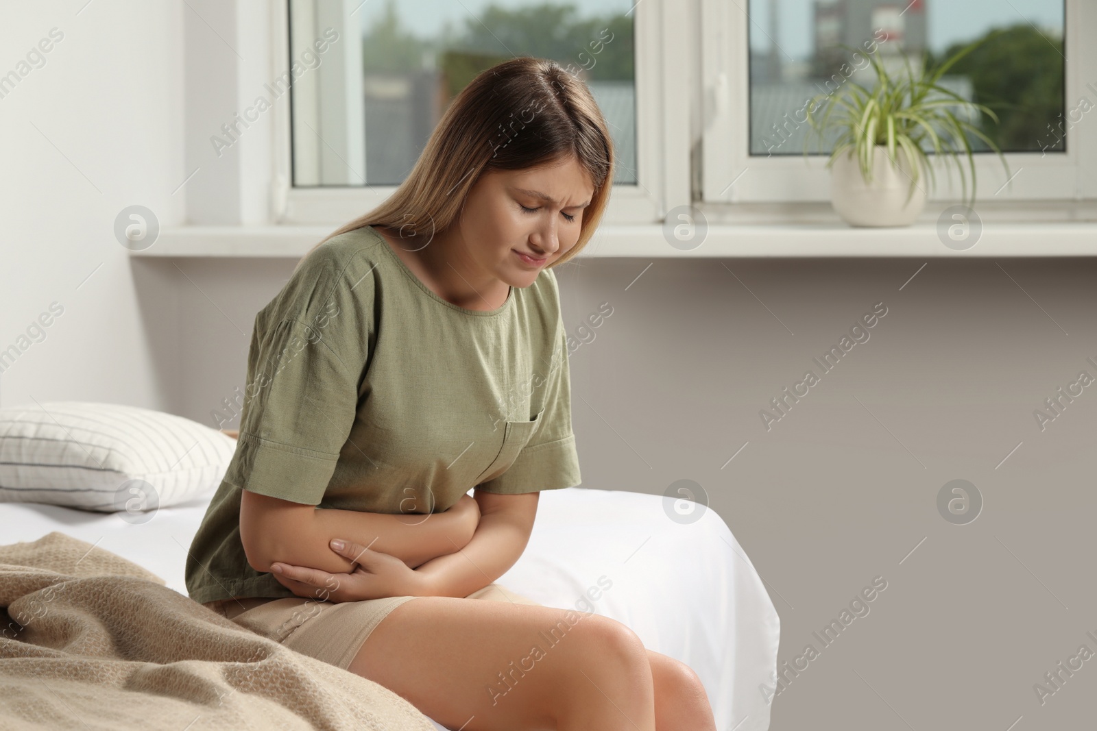 Photo of Young woman suffering from menstrual pain on bed at home, space for text