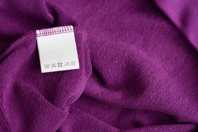 Photo of White clothing label with care information on purple garment, top view