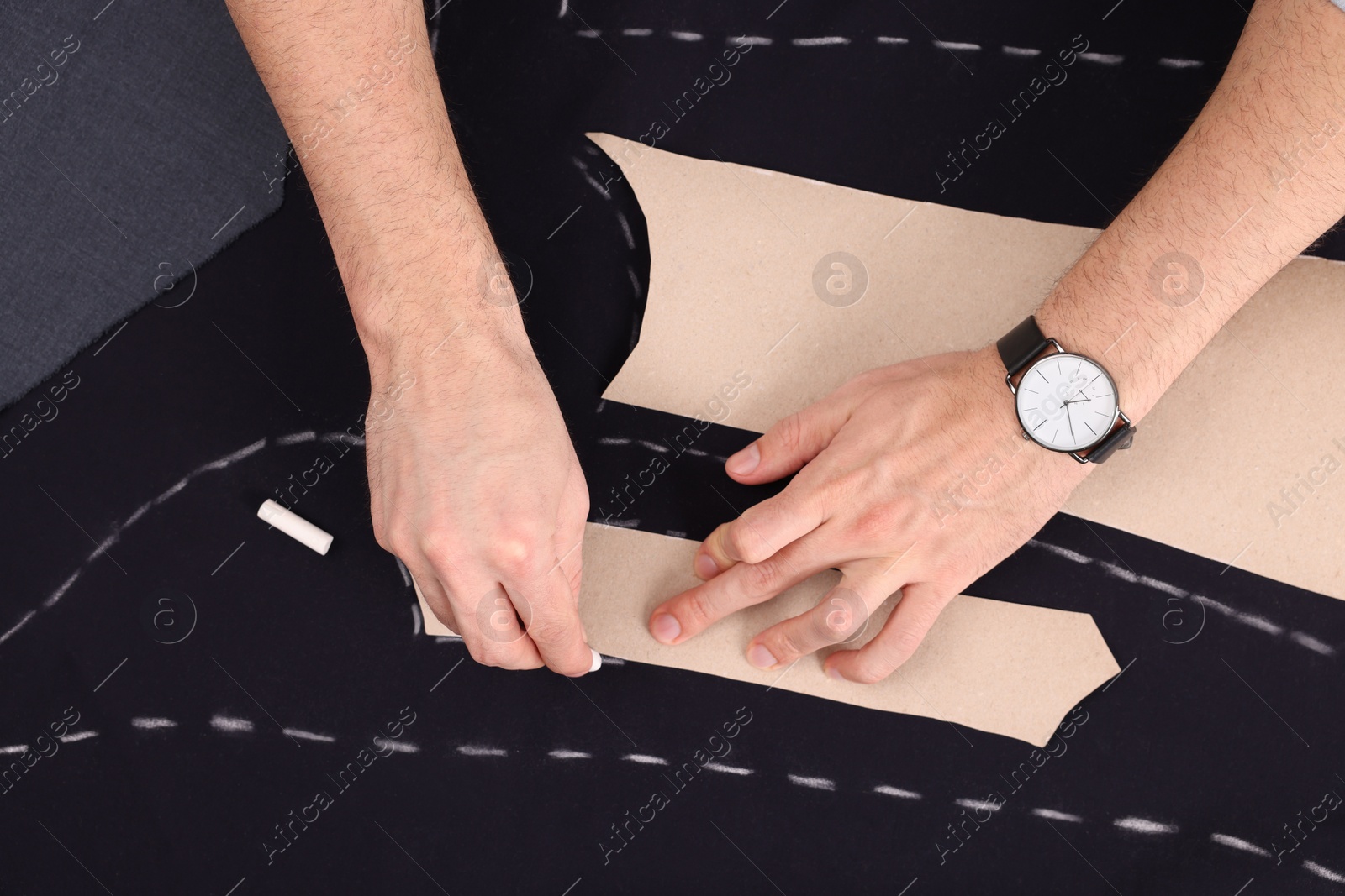 Photo of Tailor marking sewing pattern on fabric with chalk at table, top view