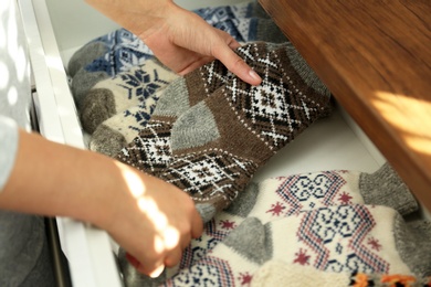 Photo of Woman taking warm knitted socks out of drawer indoors, closeup