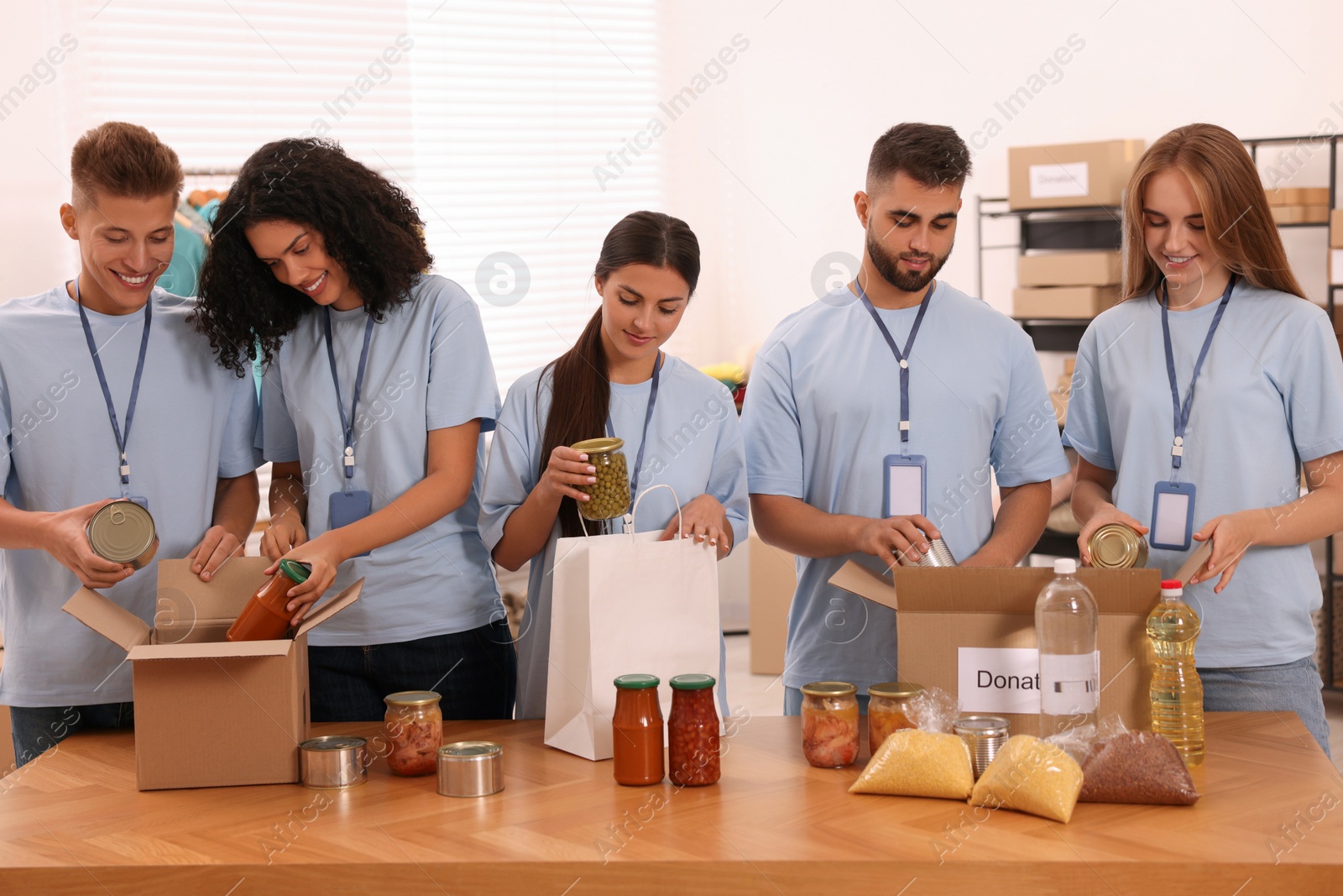 Photo of Group of volunteers packing food products at table in warehouse