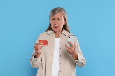 Photo of Worried woman with credit card and smartphone on light blue background. Be careful - fraud