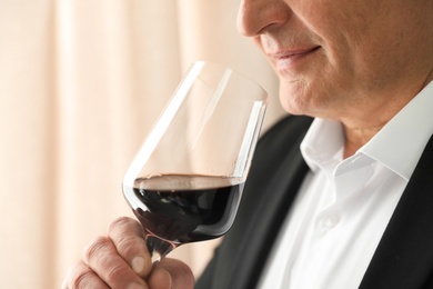 Senior man with glass of wine indoors, closeup