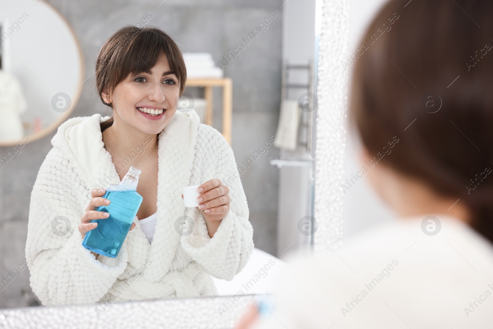 Photo of Young woman using mouthwash near mirror in bathroom