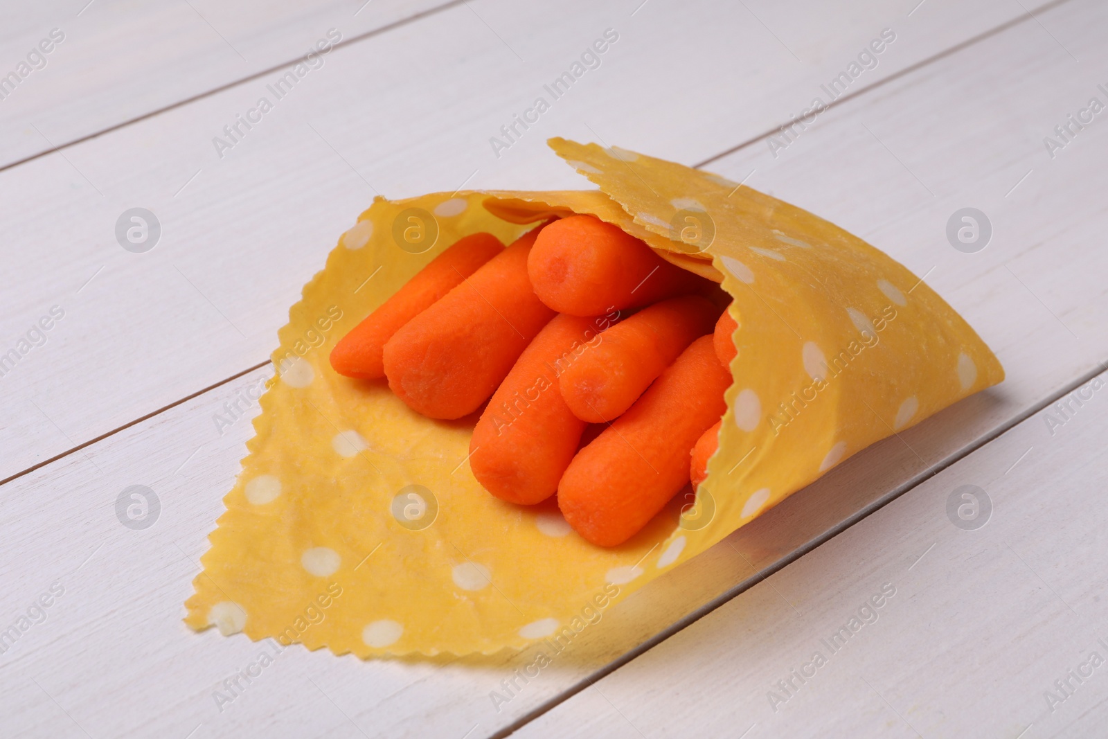 Photo of Many baby carrots in beeswax food wrap on white wooden table