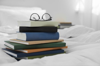 Photo of Hardcover books and glasses on bed indoors
