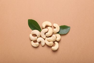 Photo of Pile of tasty cashew nuts and green leaves on pale brown background, flat lay