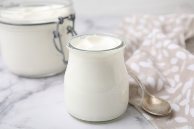 Photo of Delicious natural yogurt in glass jars and spoon on white marble table, closeup