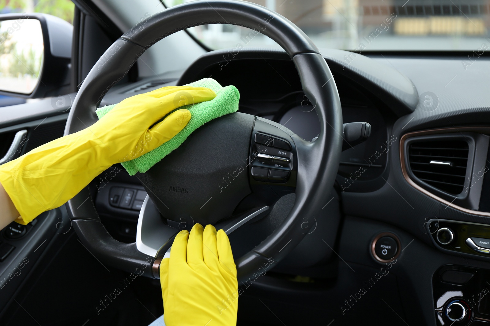 Photo of Woman cleaning steering wheel with rag in car, closeup