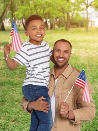 Image of 4th of July - Independence day of America. Happy father and son with national flags of United States in park