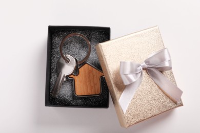 Key with trinket in shape of house and gift box on light grey background, flat lay. Housewarming party