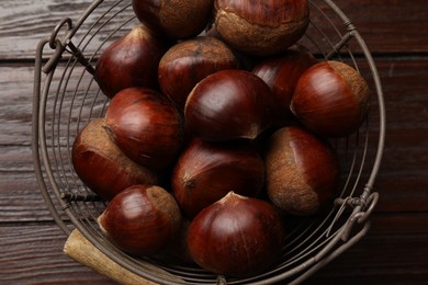 Sweet fresh edible chestnuts in metal basket on wooden table, top view